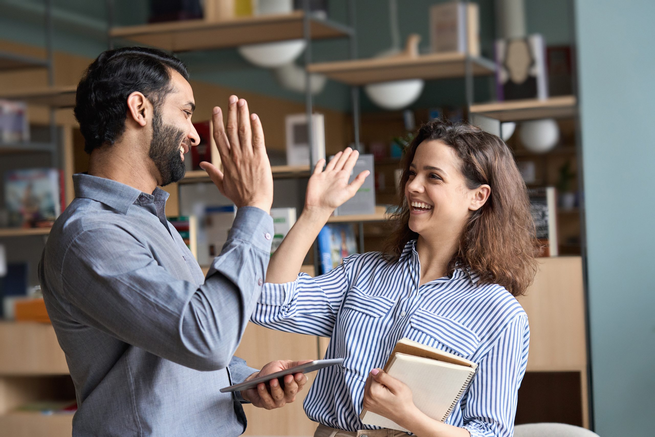 Two happy friendly diverse professionals giving high five standing in office.